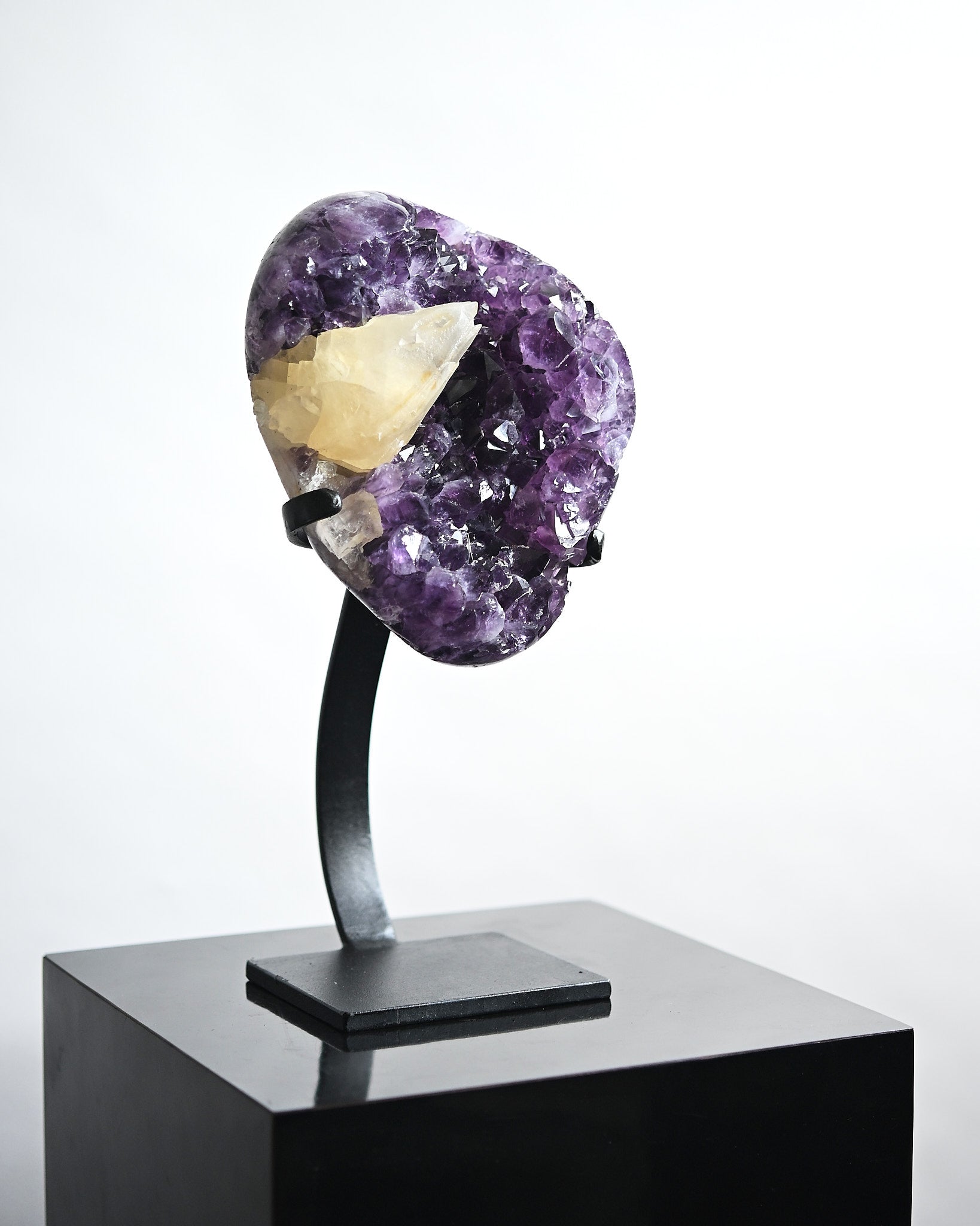 Amethyst crystal on a black stand against a white background
