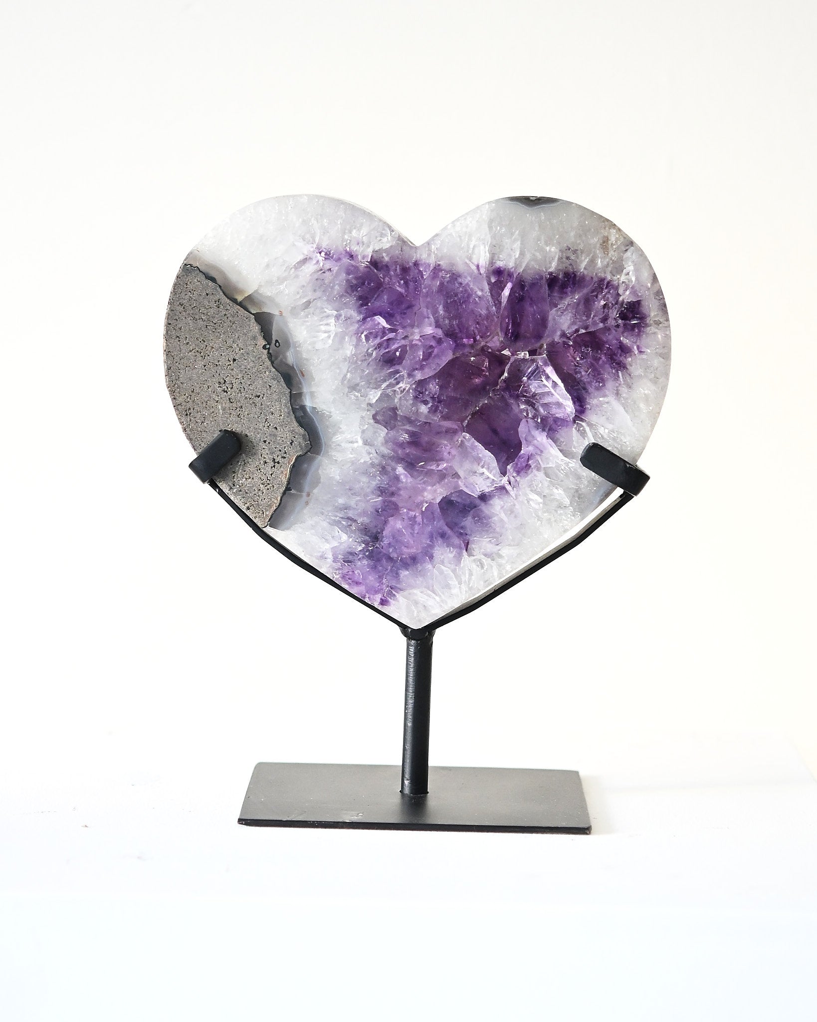 Heart-shaped crystal with purple center on a stand against a white background