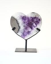 Heart-shaped crystal with purple center on a stand against a white background