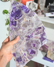 Amethyst crystal held by a hand with a blurred indoor background