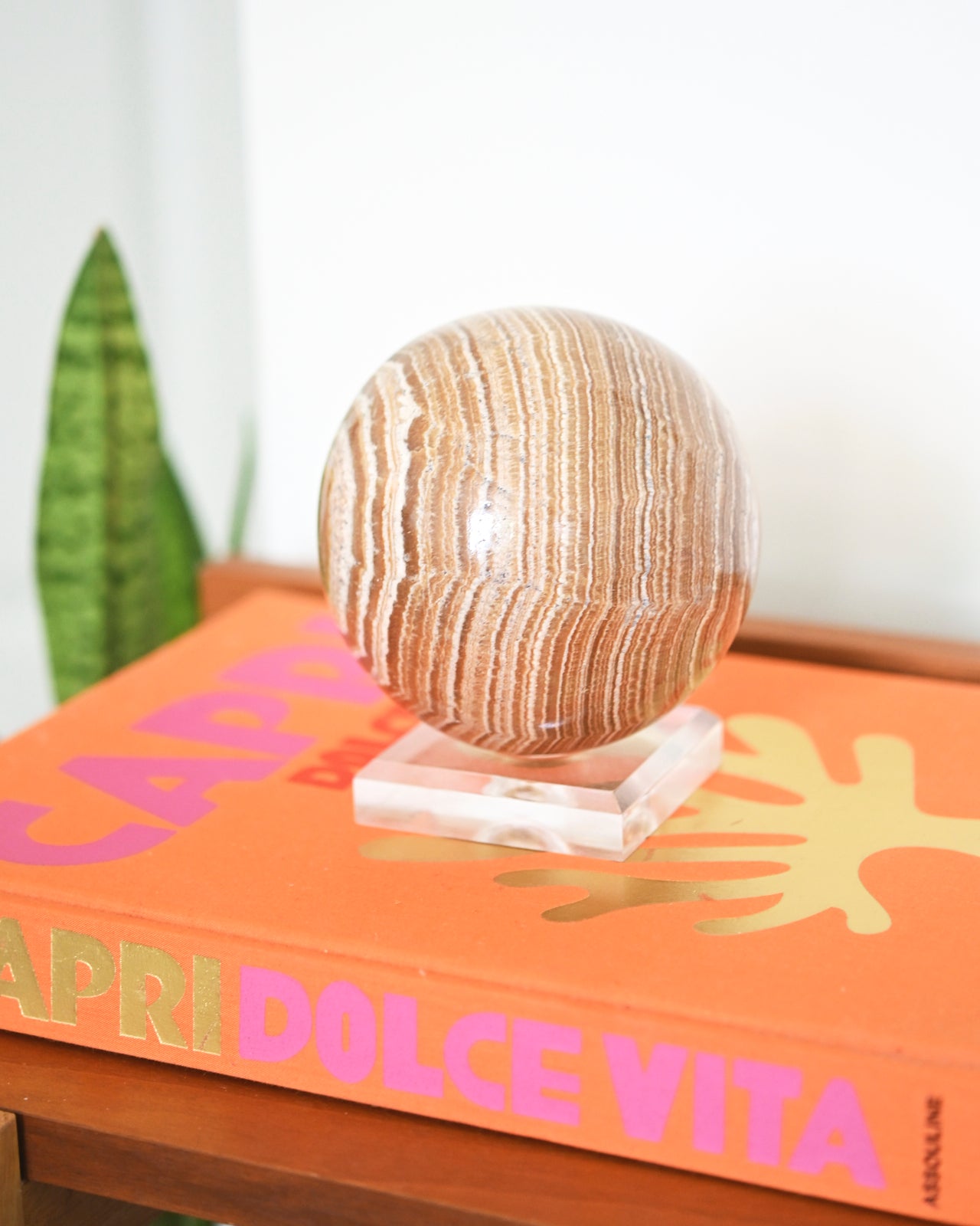 A large banded aragonite sphere displayed on top of a book titled 'DOLCE VITA'.