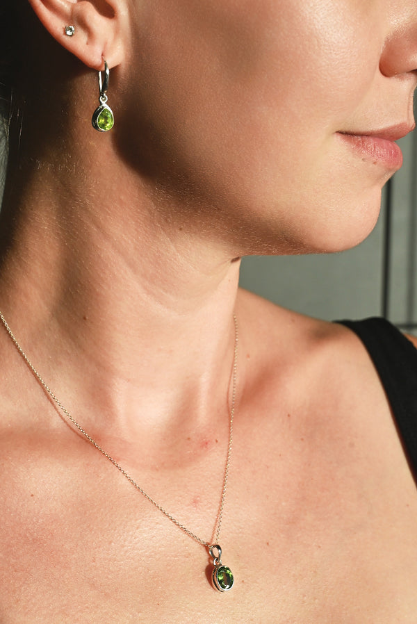 Close-up of a person wearing a necklace with a pendant and green gemstones.