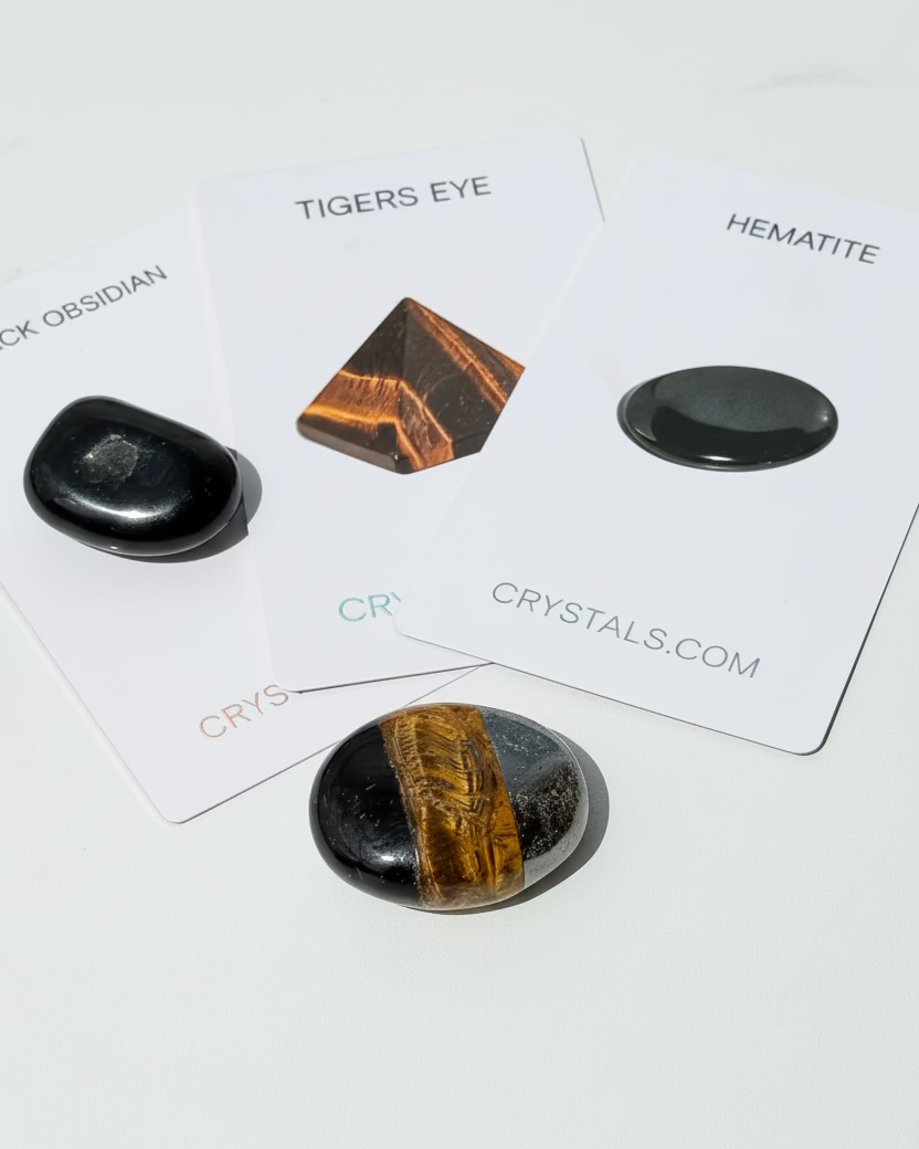 Two polished stones on cards labeled 'Tigers Eye' and 'Hematite' with 'Crys Crystals.com' branding.