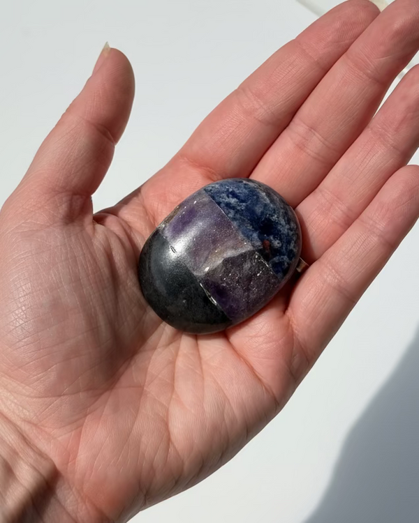 Hand holding a purple stone against a white background