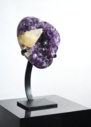 Amethyst crystal on a black stand against a white background