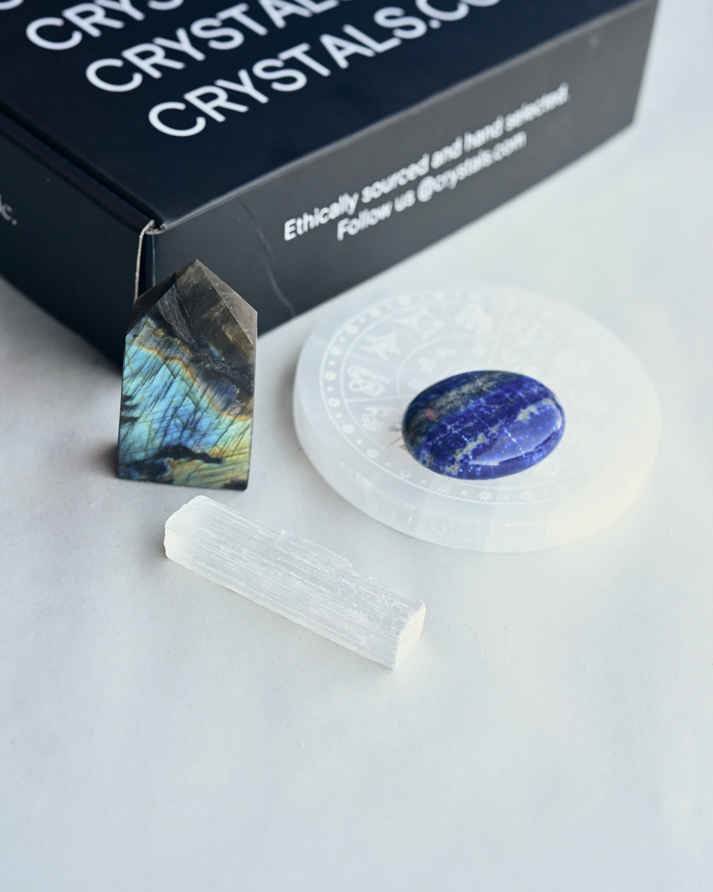 Crystal pyramid, round stone, and crystal on a white surface with 'Crystal Crystals' branding.