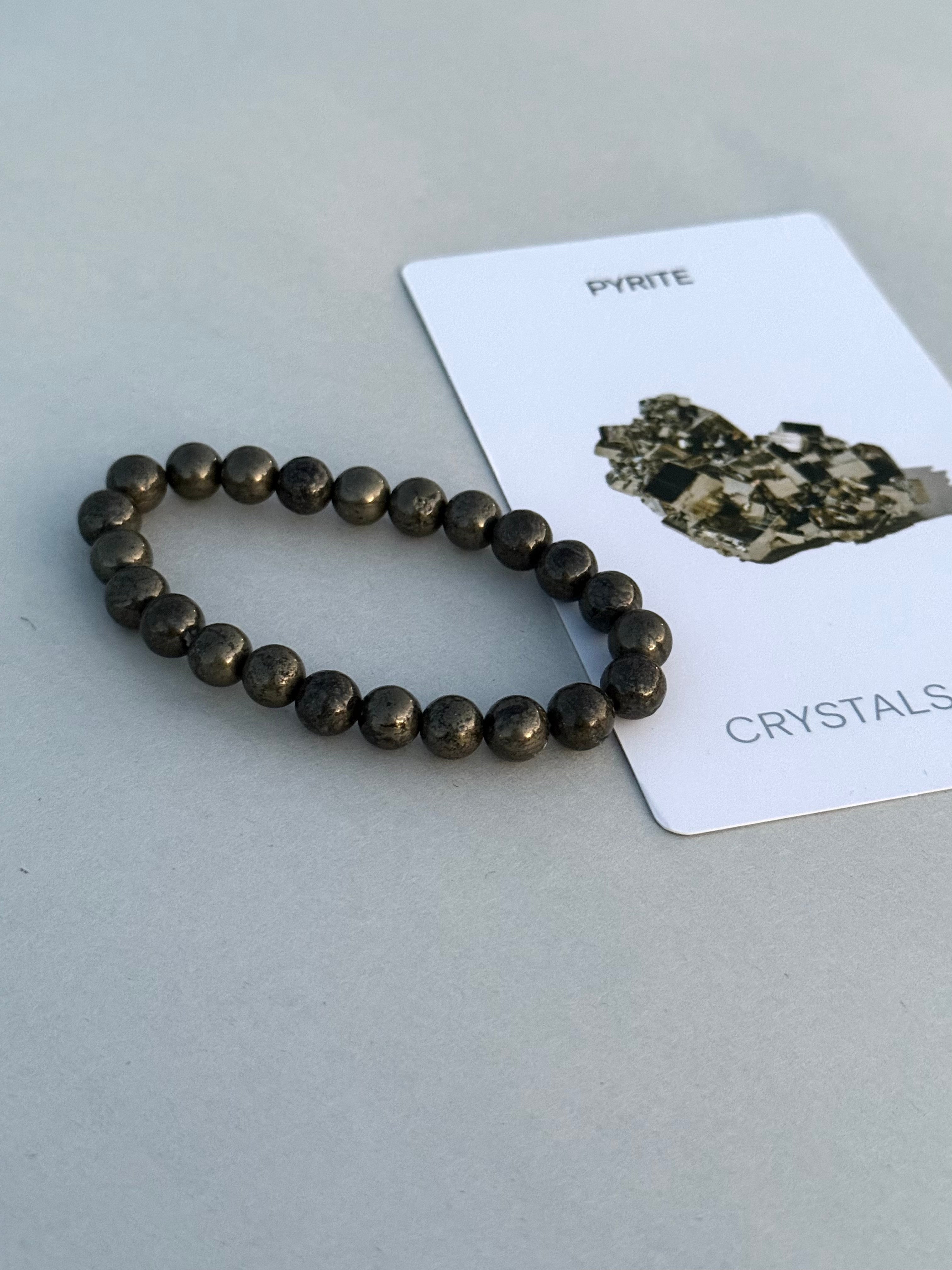 Pyrite bracelet on a gray surface with a card labeled 'Pyrite Crystals'.