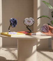 Amethyst geode crystal on a stand with another geode and a hand holding a third one on a table.