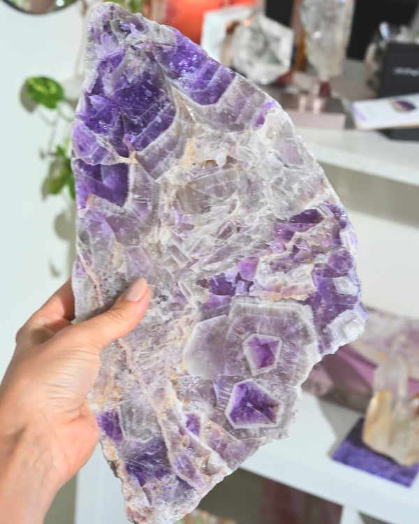 Amethyst crystal held by a hand with a blurred indoor background