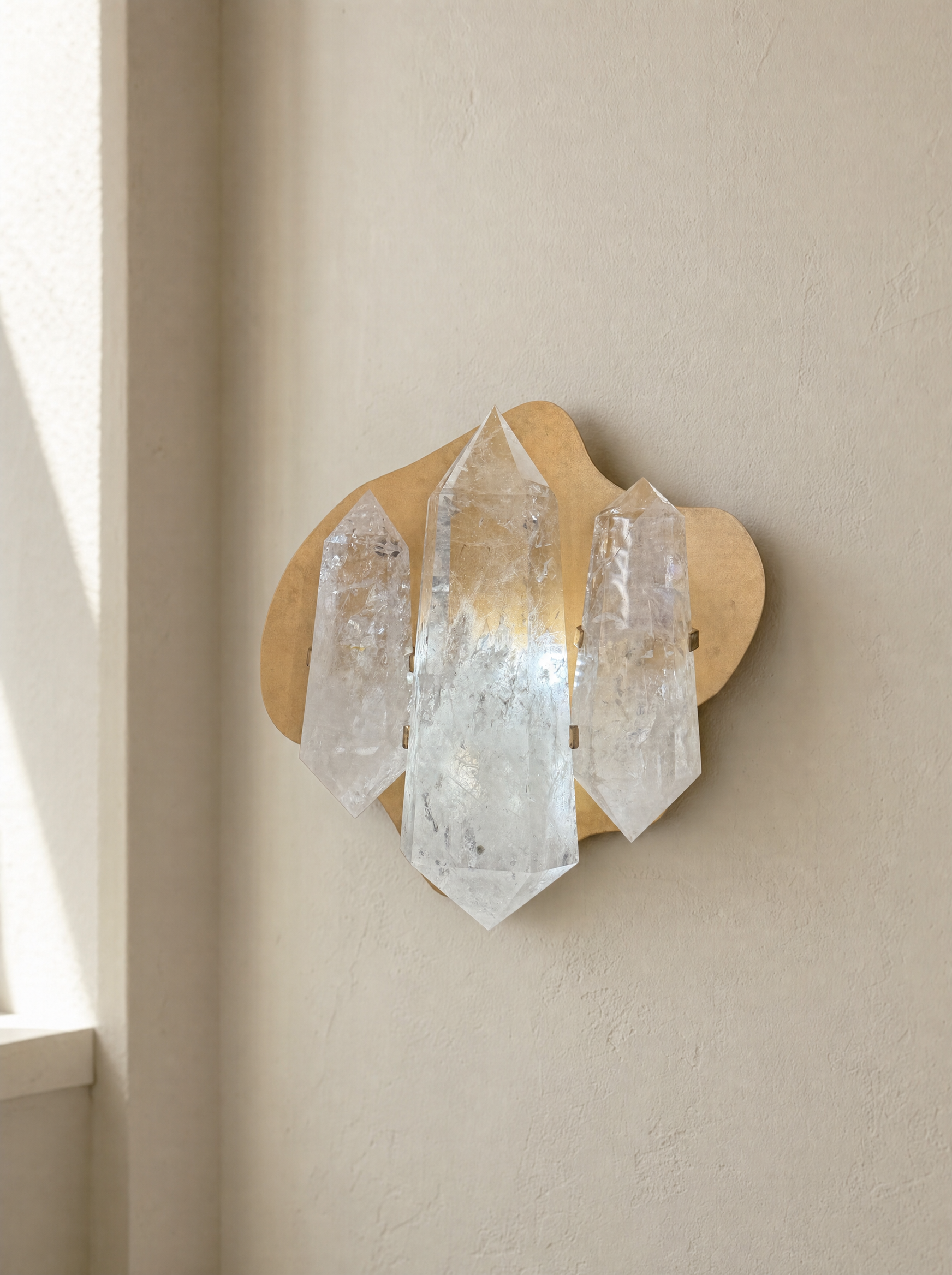 Three double terminated quartz points mounted on a plaster wall in natural light