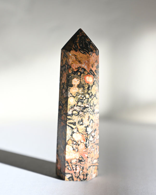 A polished jasper crystal point with a leopard skin-like pattern, displayed against a neutral background.
