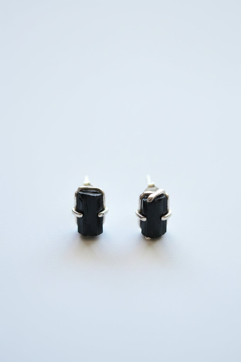 A pair of black rectangular stud earrings with gold-toned metal settings, photographed on a clean white background.