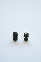 A pair of black rectangular stud earrings with gold-toned metal settings, photographed on a clean white background.