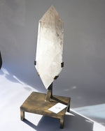 Crystal obelisk on a bronze stand against a gray background