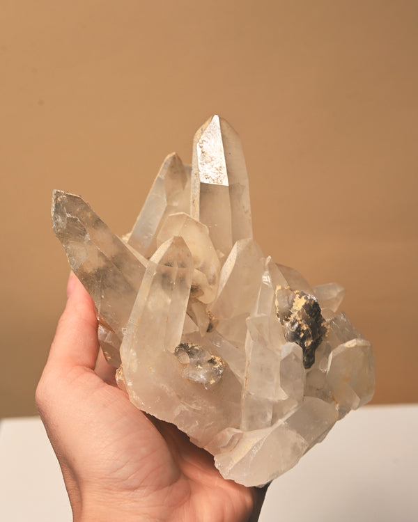 Clear crystal cluster held in a hand against a beige background