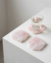 Rose quartz coaster set with glass of water on white table - natural pink crystal slab coasters from Brazil