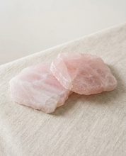 Pair of natural rose quartz crystal coasters with polished face and raw edge on linen
